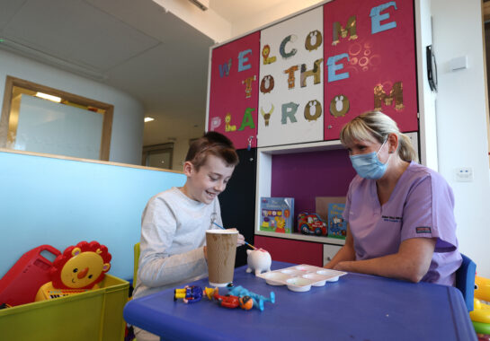 A child painting sat next to a play specialist at Alder Hey Children's Hospital