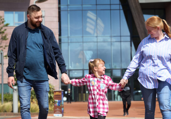 Parents and child holding hands as they leave the hospital