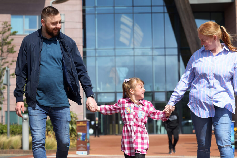 Parents and child holding hands as they leave the hospital